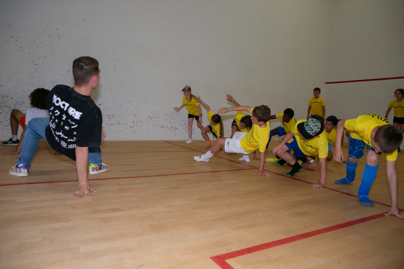 Gymles op een basisschool: kinderen doen samen met een vakdocent een beweegoefening op de sportzaalvloer